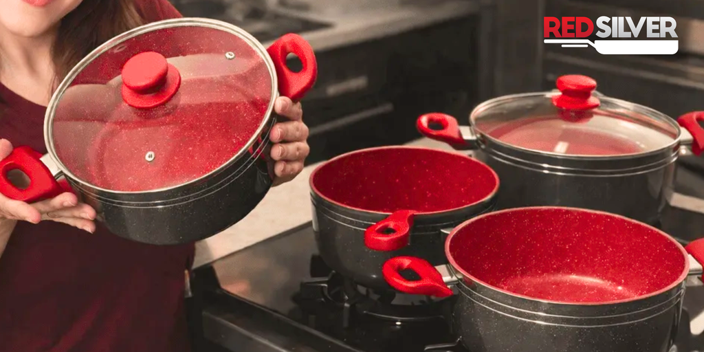 RedSilver é boa? Panelas RedSilverfuncionam e valem a pena? 5 Mulher segurando uma panela RedSilver com tampa de vidro e cabos vermelhos, ao lado
de outras panelas do kit sobre o fogão.